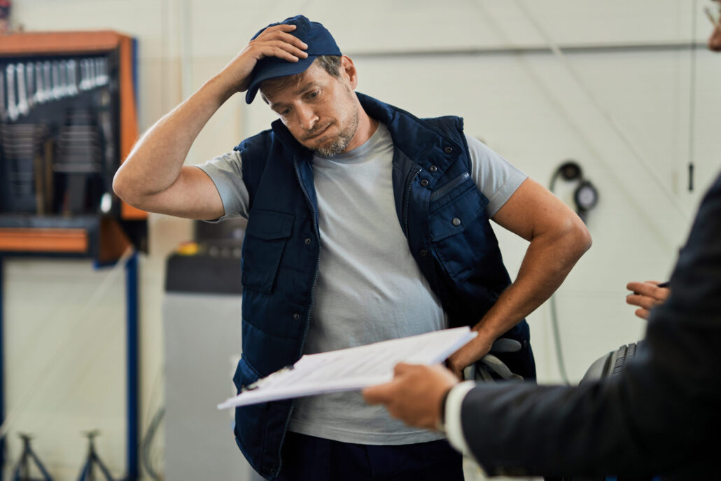  A stressed operations manager in a warehouse, holding his head, surrounded by boxes, representing the overwhelming pressure of manual year-end inventory.